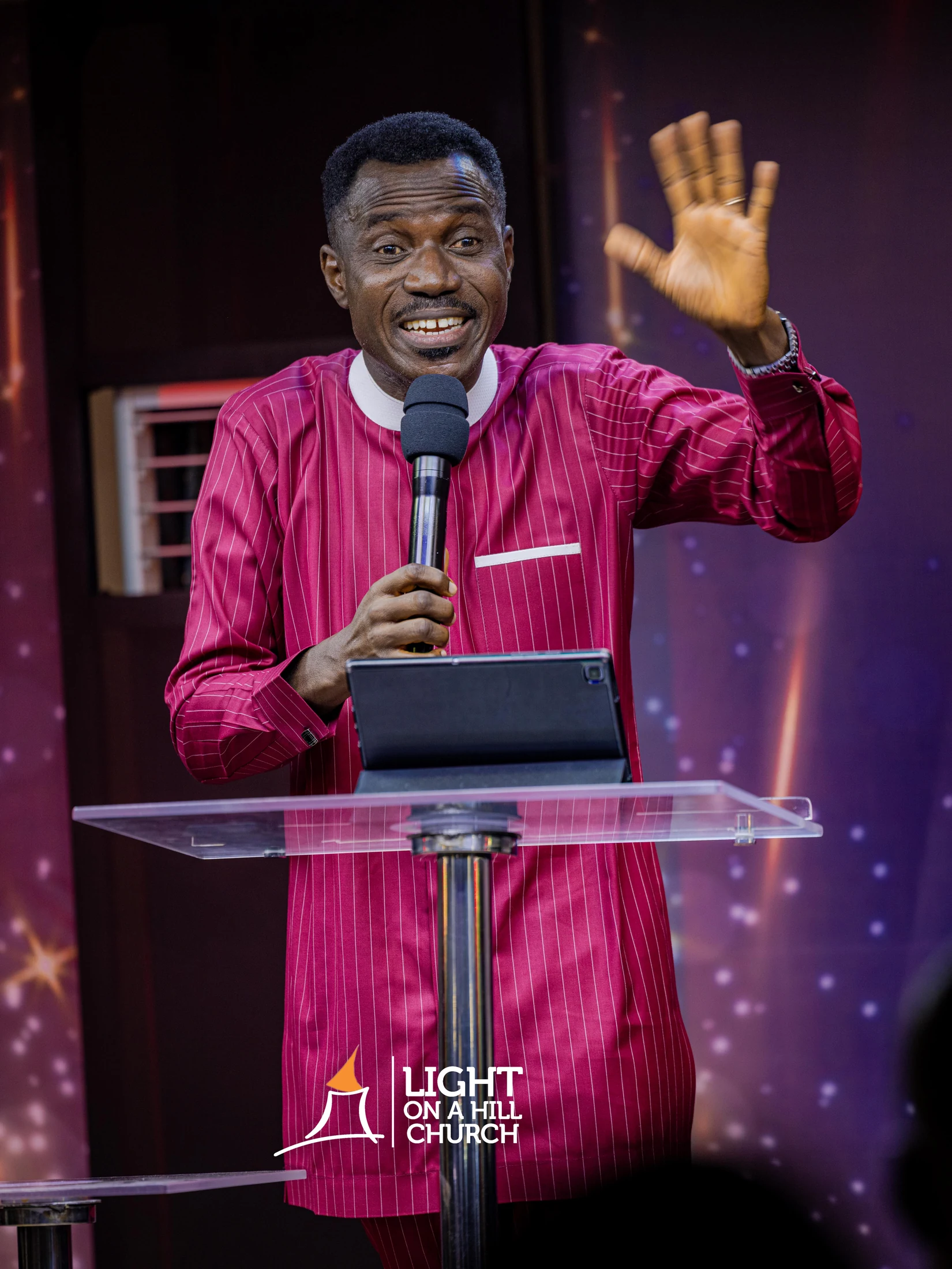 Kayode Braimoh speaking in a magenta tunic, with his face above the card text.