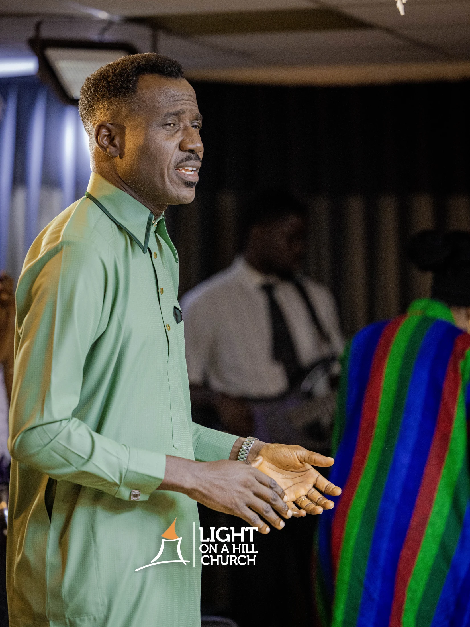 Kayode Braimoh speaking to an audience in a green shirt.